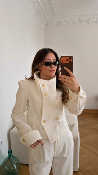 Off-white, high-neck jacket and trousers set with gold button detail and shoulder pads.
