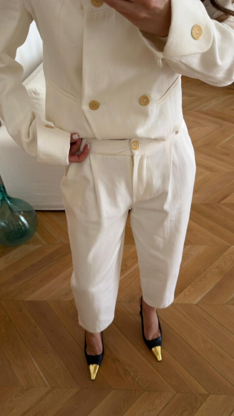 Off-white, high-neck jacket and trousers set with gold button detail and shoulder pads.