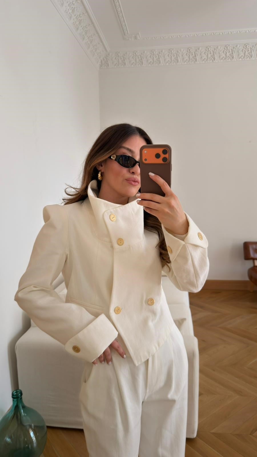 Off-white, high-neck jacket and trousers set with gold button detail and shoulder pads.