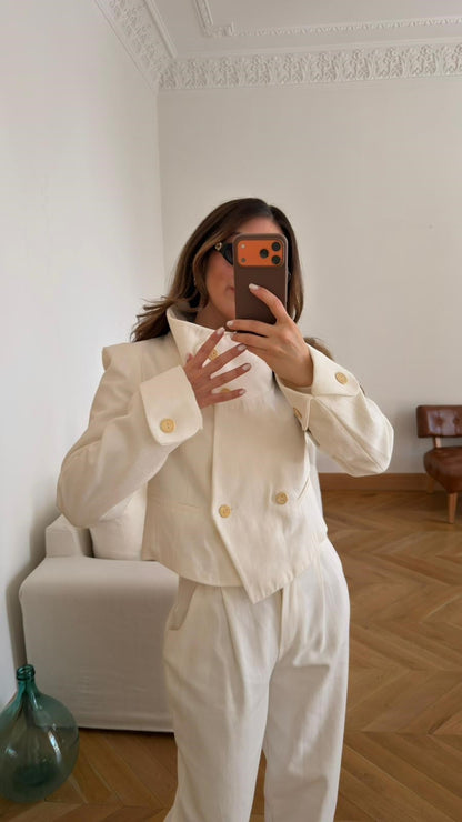 Off-white, high-neck jacket and trousers set with gold button detail and shoulder pads.
