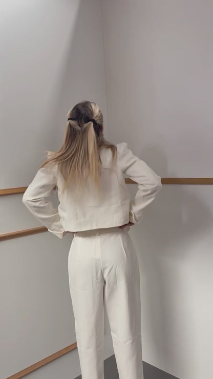 Off-white, high-neck jacket and trousers set with gold button detail and shoulder pads.